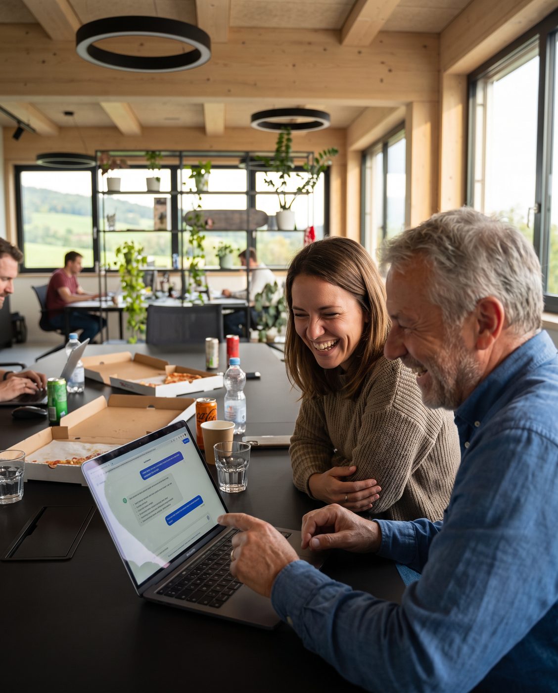 Zwei Kolleg:innen lachen über etwas auf dem Laptop.